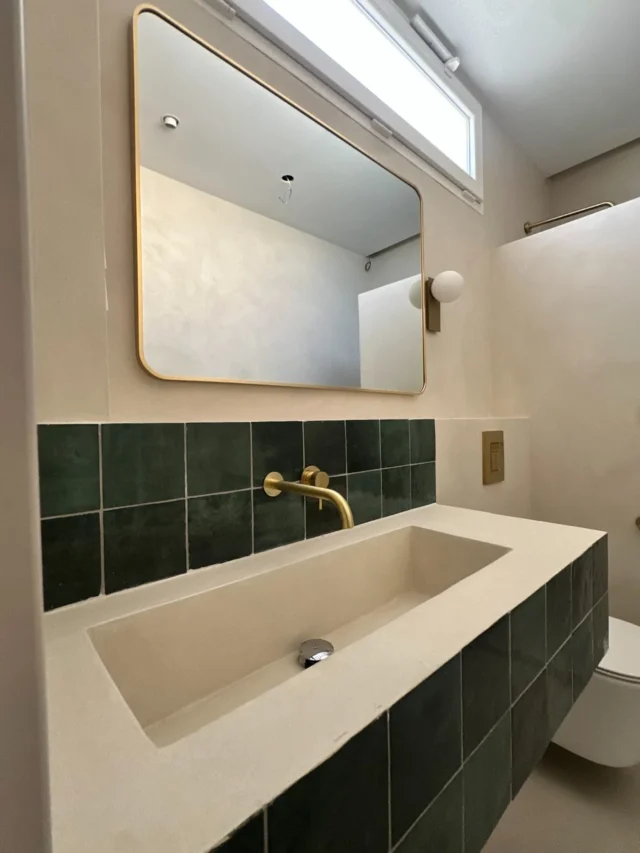 Baño con lavabo integrado, azulejo verde y grifería de latón