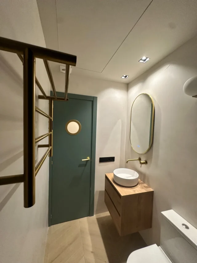 Baño con puerta verde, mueble de madera y detalles de latón