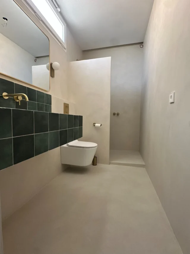 Baño con revestimiento continuo, azulejo verde y detalles de latón